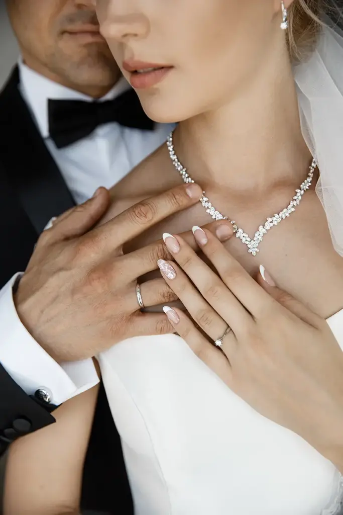 Detailaufnahme des Colliers der Braut, während die Hand des Bräutigams dezent sichtbar ist