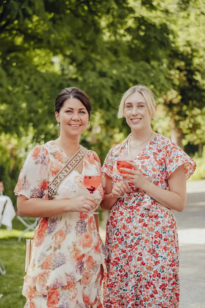 Hochzeitsplanerin Nancy und ihre Assistentin Julia stehen mit einem alkoholfreien sommerlichen Cocktail in einem Garten