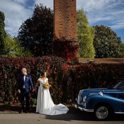 Hochzeitspaar steht neben einem Oldtimer in herbstlicher Atmosphäre und blickt in entgegengesetzte Richtungen
